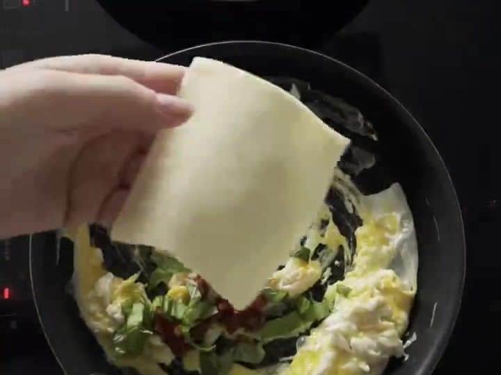 Italian Breakfast Tacos with Sun-Dried Tomatoes and Mozzarella 5 A slice of mozzarella melting on top of scrambled eggs with sun-dried tomatoes in a black pan.