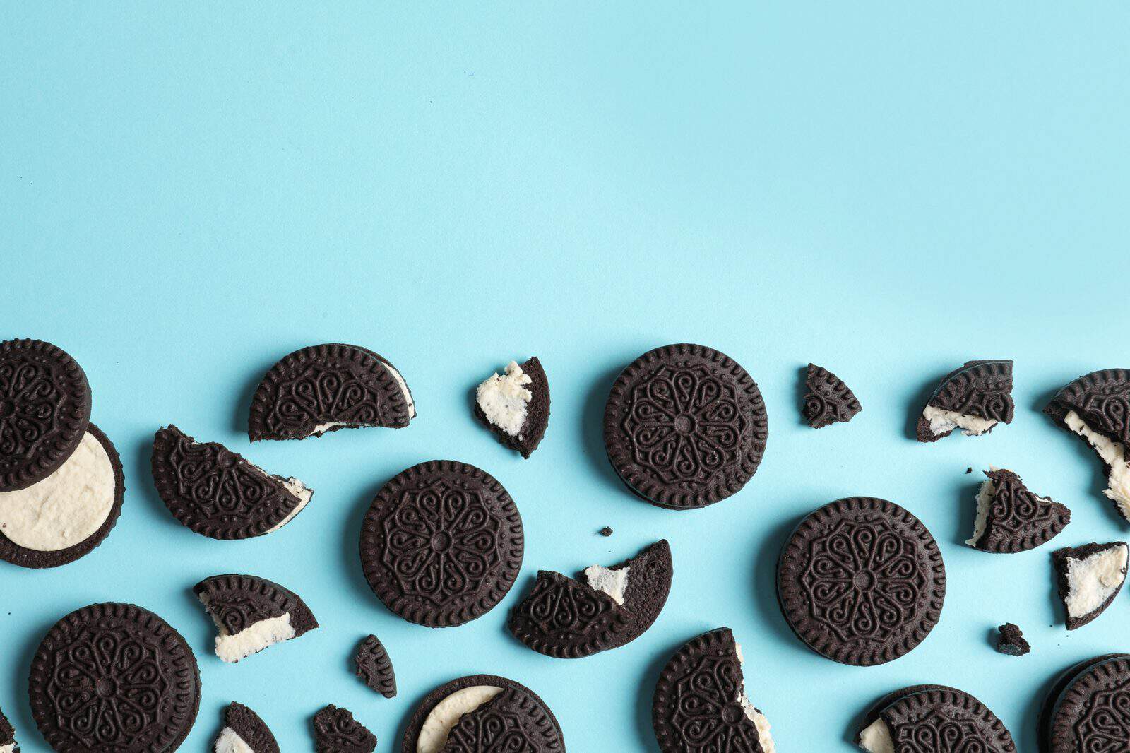 Oreo sandwich cookies, whole and broken, on a blue background