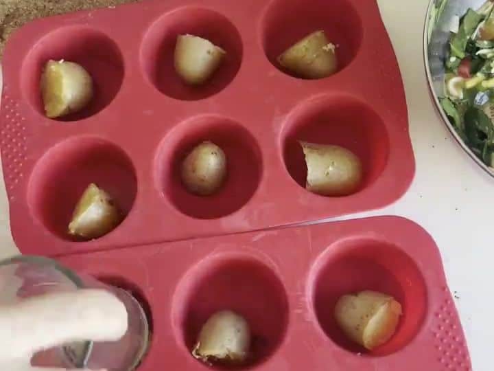 Cottage Cheese Veggie Egg Bites with a Potato Crust 5 A small cup is pressing a boiled potato piece flat into a red silicone muffin cup to form a crust.
