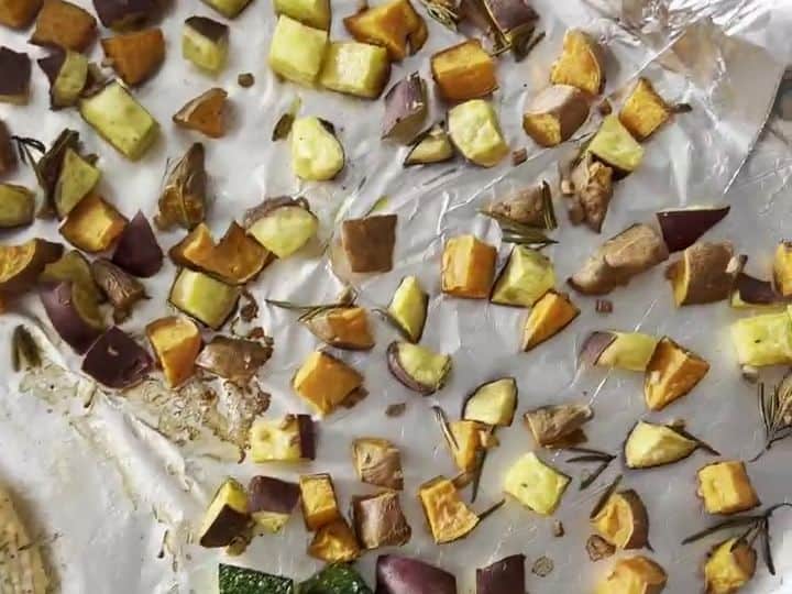 A baking sheet lined with foil holds roasted sweet potato cubes and zucchini pieces, ready to come out of the oven.