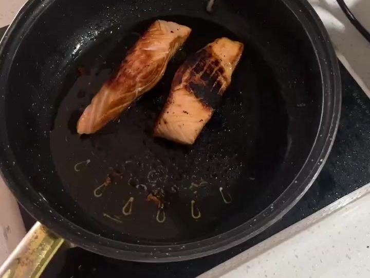 Sweet and Spicy Salmon Bowl Gets Its Crunch from Mango and Cucumber 5 Two salmon fillets sear in a dark pan with visible golden-brown crust on the stovetop.