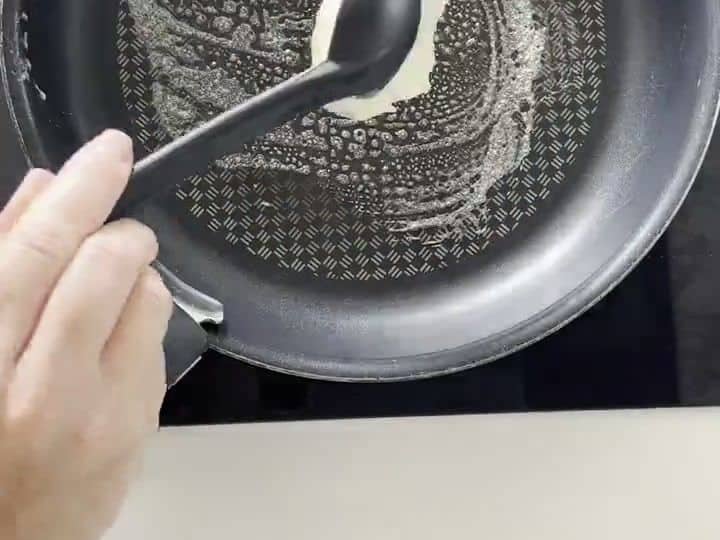 A spoon is pouring thick pancake batter onto a hot skillet, forming a round pancake.