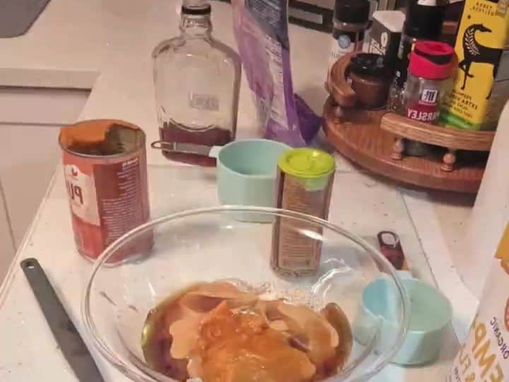 A glass bowl holds a thick pumpkin-colored dough with a spatula resting beside it.