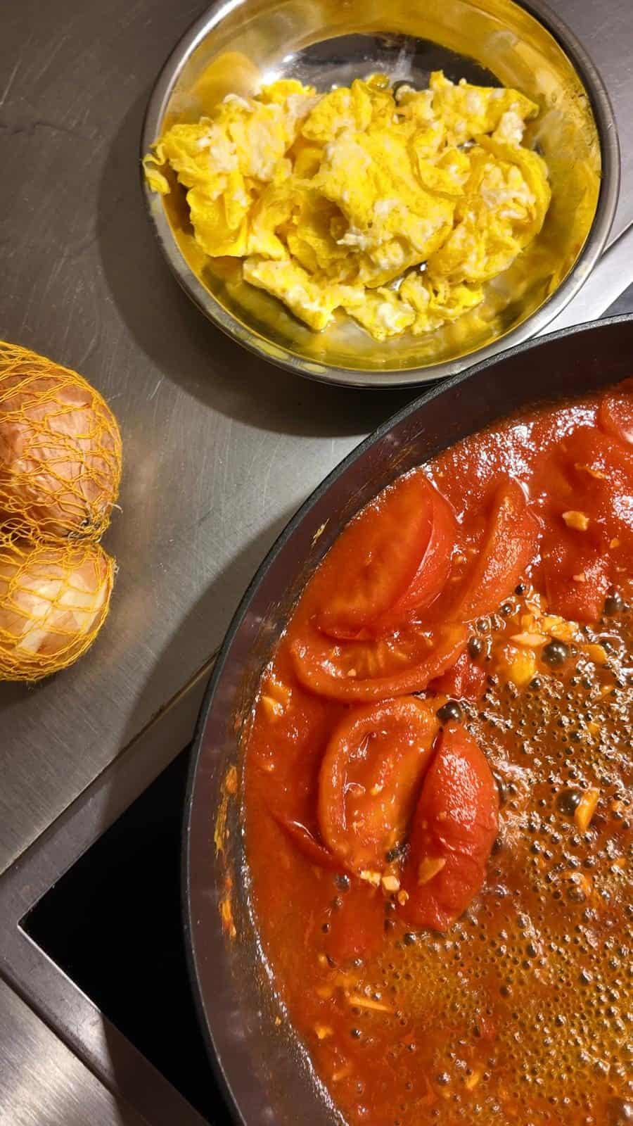 Tomato sauce cooking on stove, with eggs on the side.