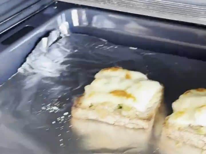 How to Make Tuna Melts with Pickles and Hot Sauce 6 Two tuna melt sandwiches sit on a baking sheet inside the oven with bubbling, golden-browned melted cheese on top.