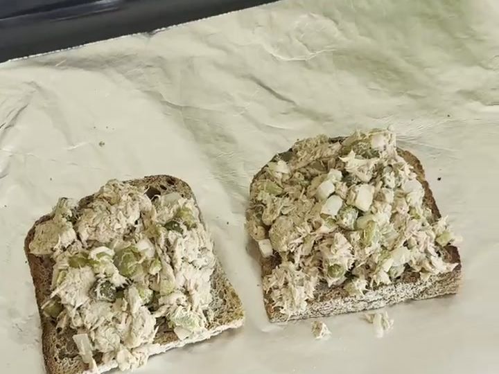 How to Make Tuna Melts with Pickles and Hot Sauce 5 Tuna salad mixture is spread evenly across two slices of bread on a foil-lined baking sheet, not yet topped with cheese.